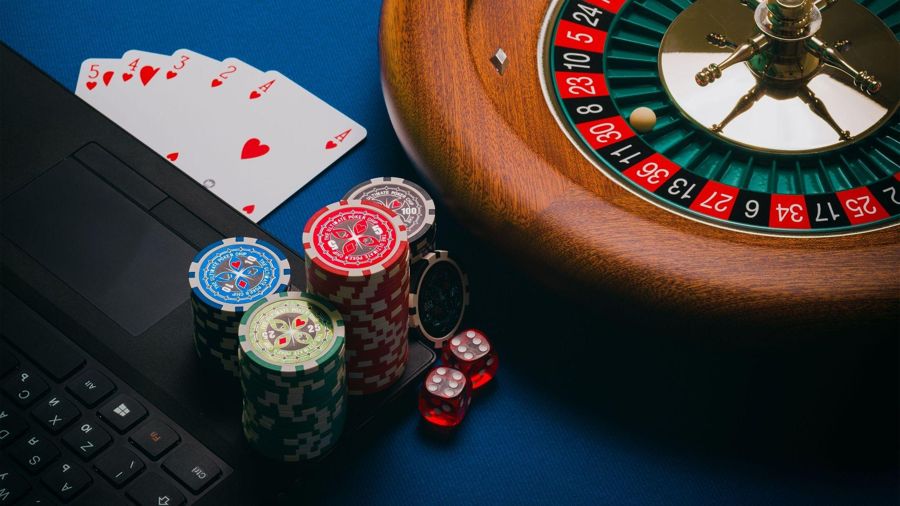 Roulette wheel, poker chips, playing cards, and laptop representing online casino gaming and gambling.